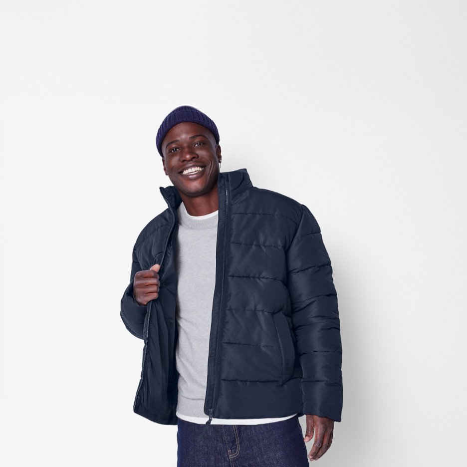 Mand i mørkeblå pufferjakke, grå sweater og mørke jeans.