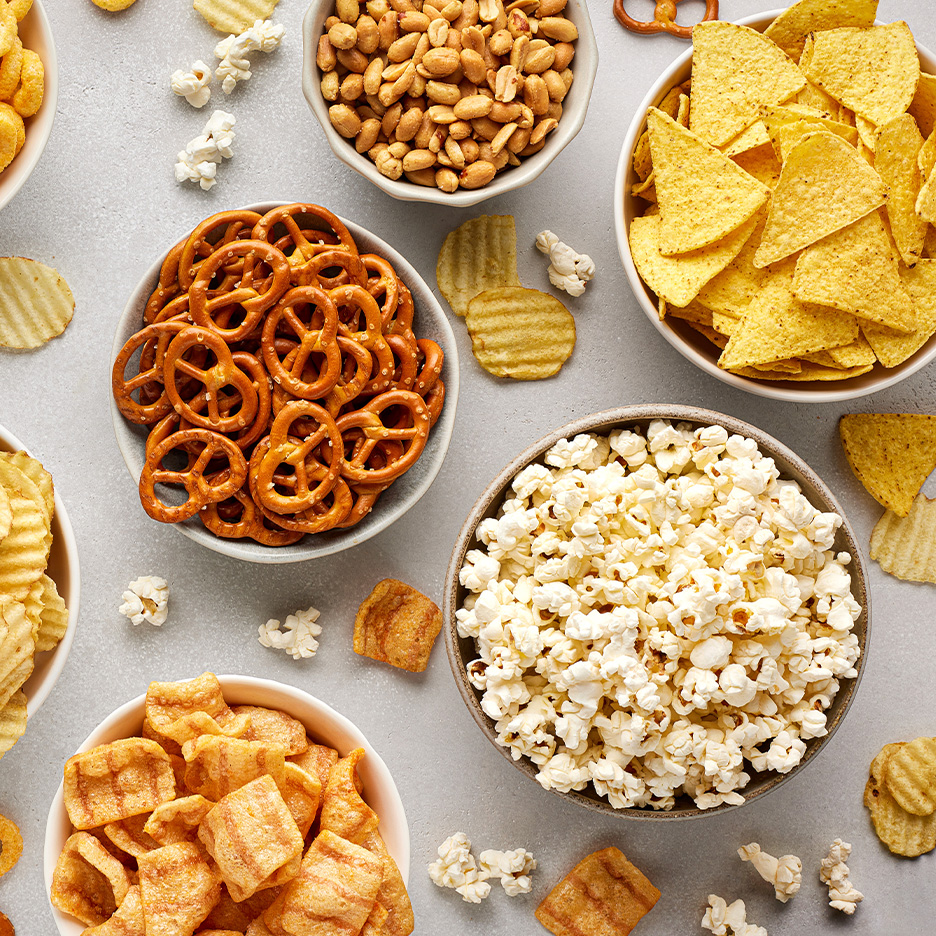 En række snacks, herunder popcorn, pretzels, tortillachips, peanuts og kartoffelchips.