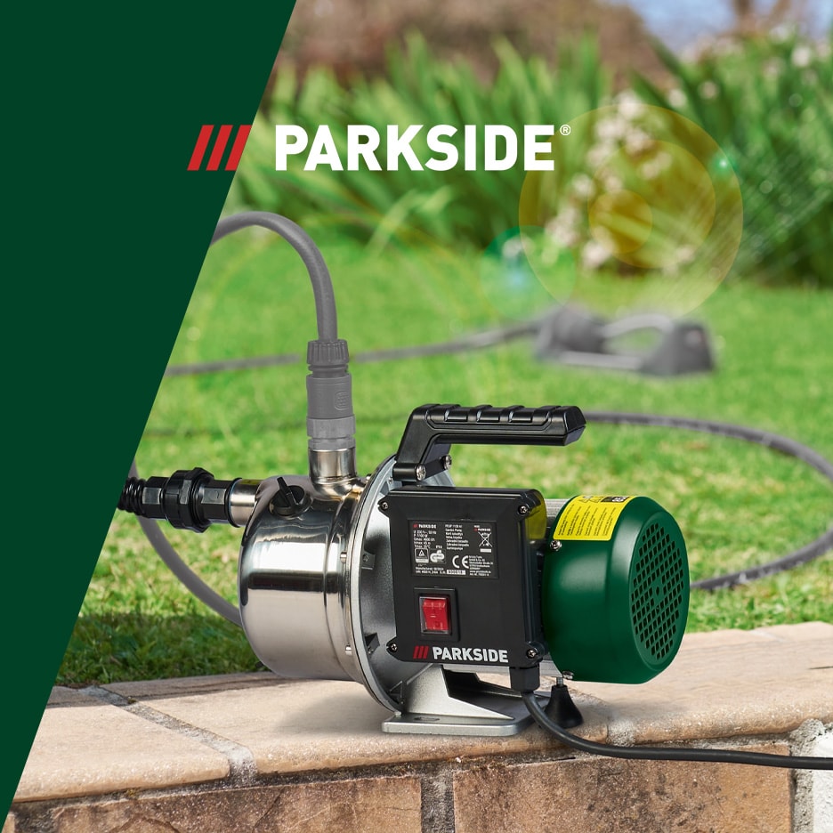 Vandpumpe i rustfrit stål med grøn motor og sort håndtag, placeret på en murstensoverflade i en have.