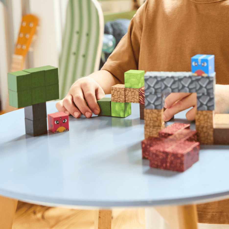 Barn leger med farverige byggeklodser, der forestiller et landskab med træer og en buegang.