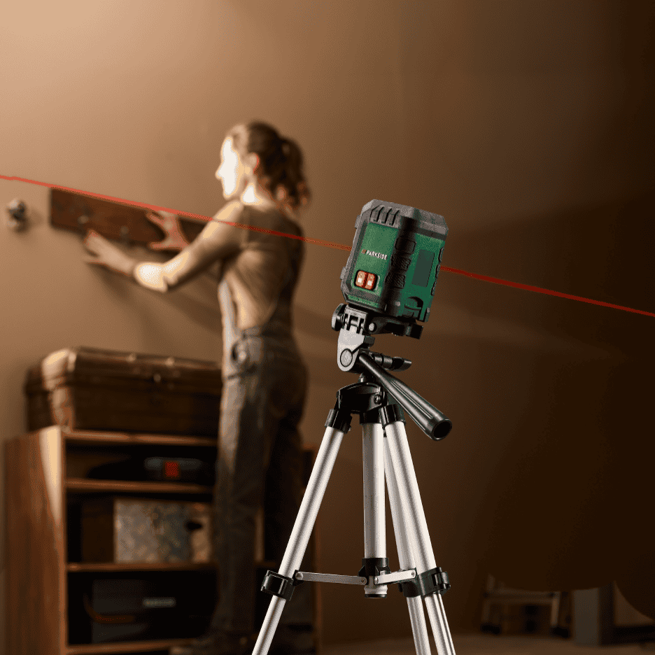 En kvinde bruger et laserniveau på et stativ til at hænge en hylde op.