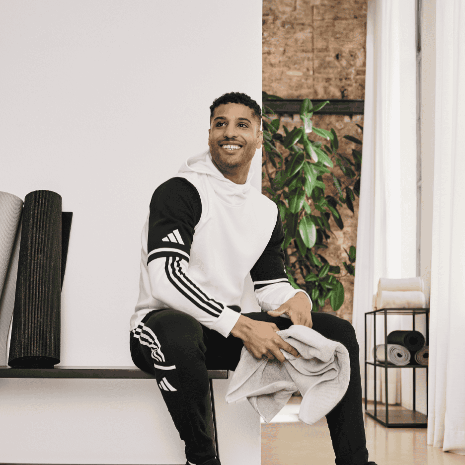 Mand i træningstøj sidder på en bænk med et håndklæde og smiler.