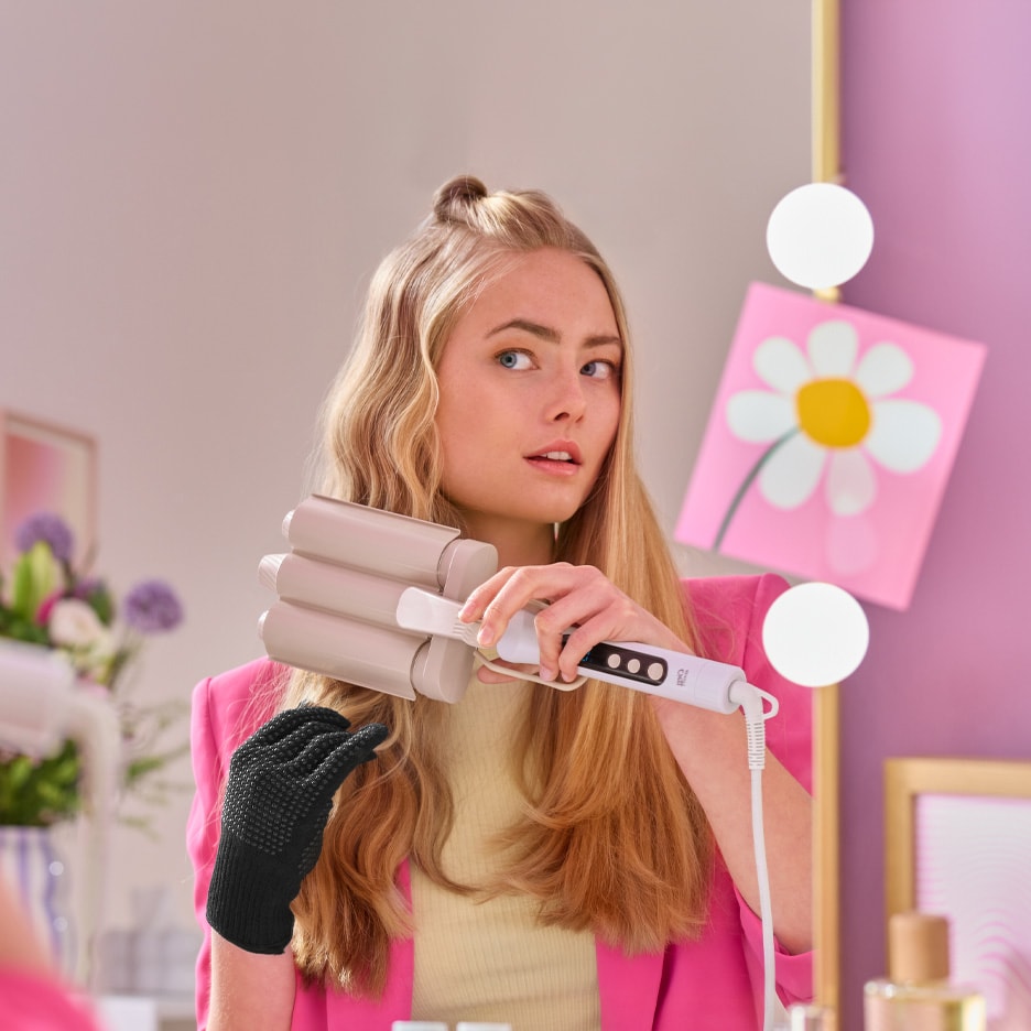 Ung kvinde med bølgejern og varmebestandig handske, der laver bølger i sit blonde hår.