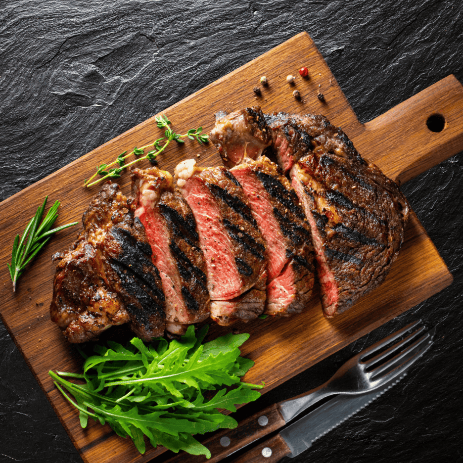 Skåret grillet bøf med rosmarin, timian og rucola på et træskærebræt.