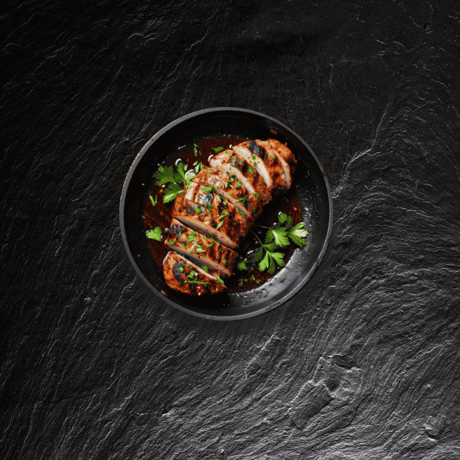 Skiver af grillet svinemørbrad med persille og sauce i en sort pande på en mørk skiferoverflade.