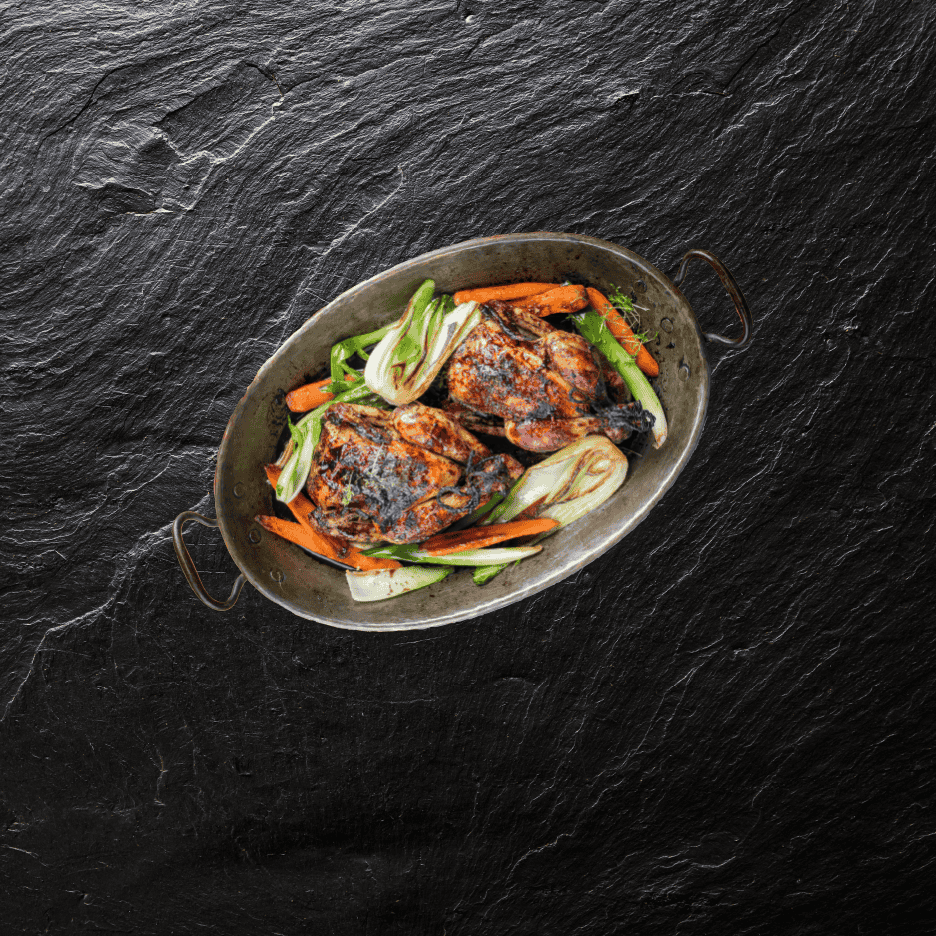 Grillet kylling med gulerødder og bok choy i en oval pande på en mørk skiferoverflade.