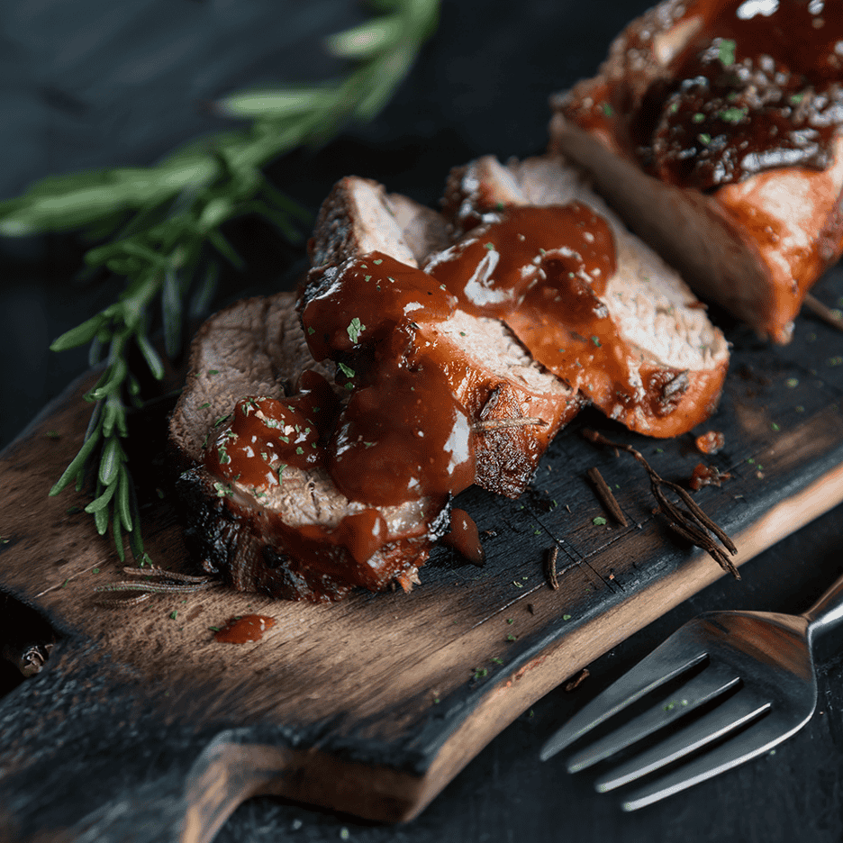 Skiver af stegt kød med brun sauce og rosmarin på et træskærebræt.