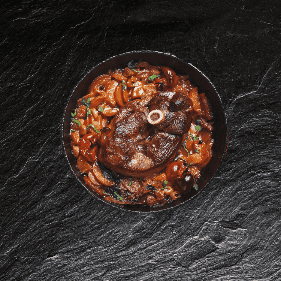 Braiseret lammekølle med grøntsager i en sort skål på en mørk stenoverflade.