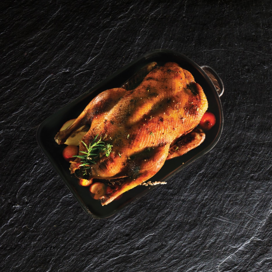 Helstegt and med rosmarin og æbler i en sort bradepande på mørk baggrund.