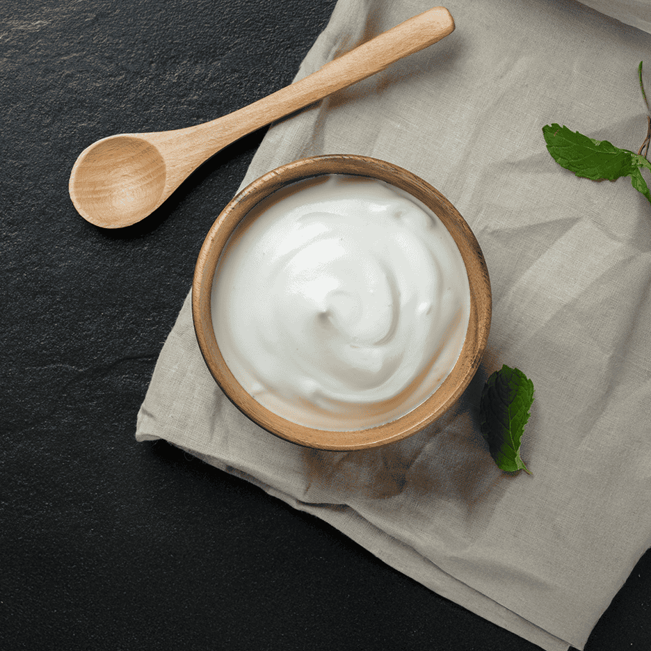 Skål med yoghurt, træske og mynteblade på et gråt klæde.