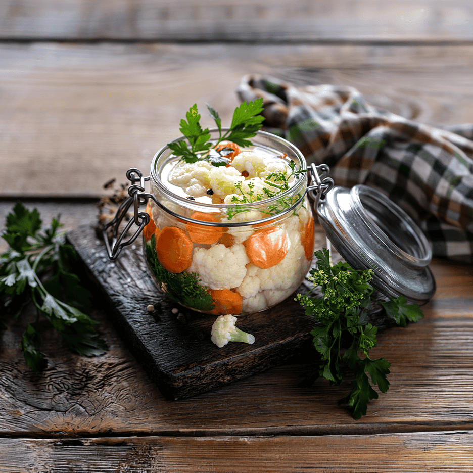 Syltede blomkål og gulerødder i et glas på et træbord.