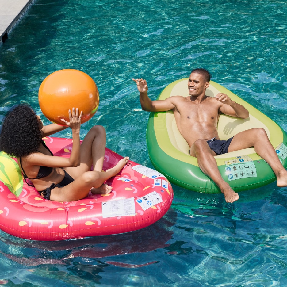 To personer slapper af i en pool på en jordbær- og en avocadopoolmadras.