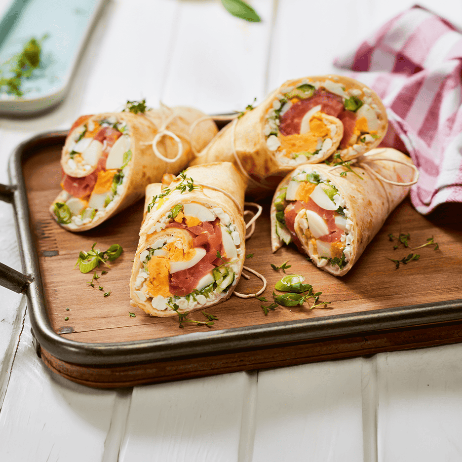 Lækre wraps med æg, laks og grønt på et træfad.