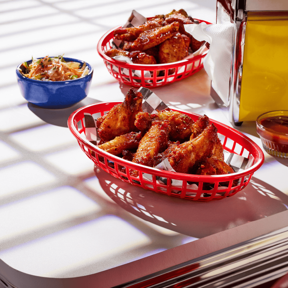 To kurve med sprøde kyllingevinger, en skål coleslaw og en dip på et bord.