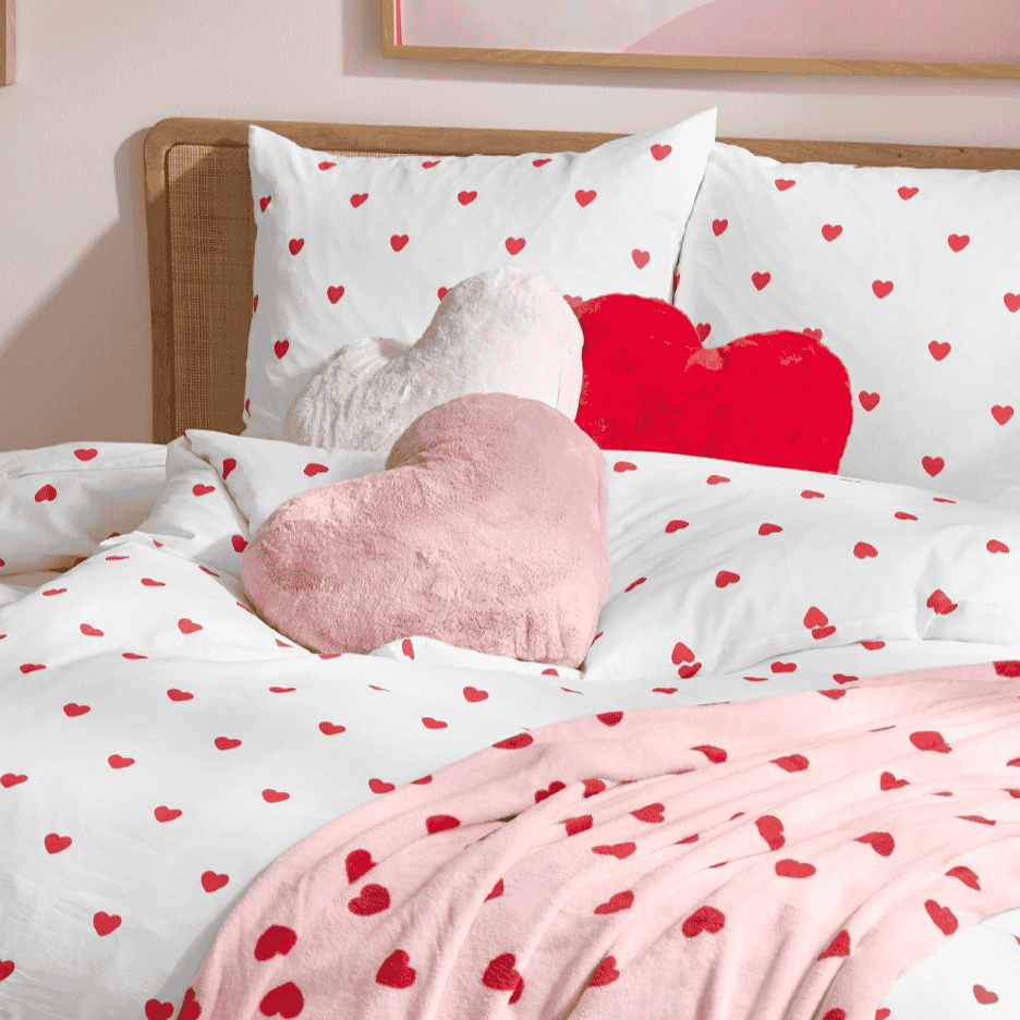 Sengesæt med hjerter og hjerteformede pyntepuder i lyserød, hvid og rød.