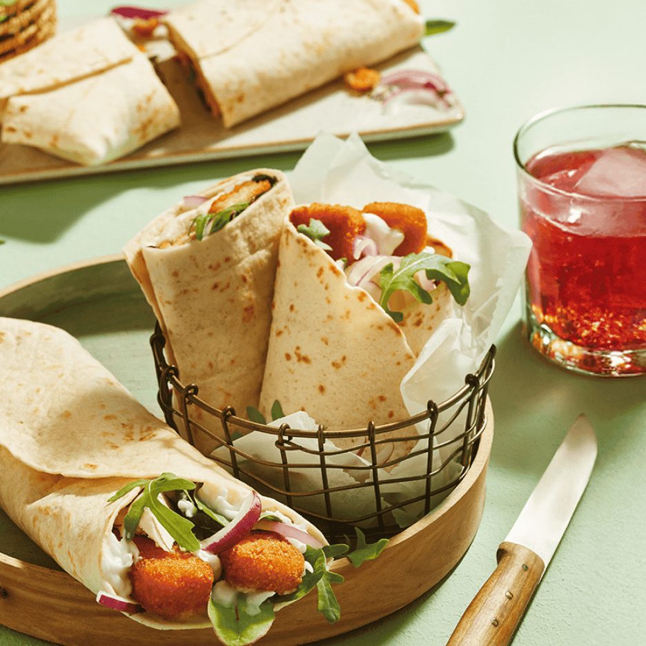 Tortillawraps med sprøde nuggets, salat, rødløg og dressing, serveret med en rød drink.