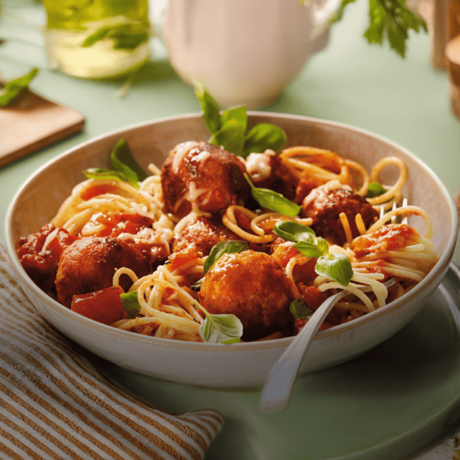 Spaghetti med kødboller, tomatsauce, basilikum og revet ost i en skål.