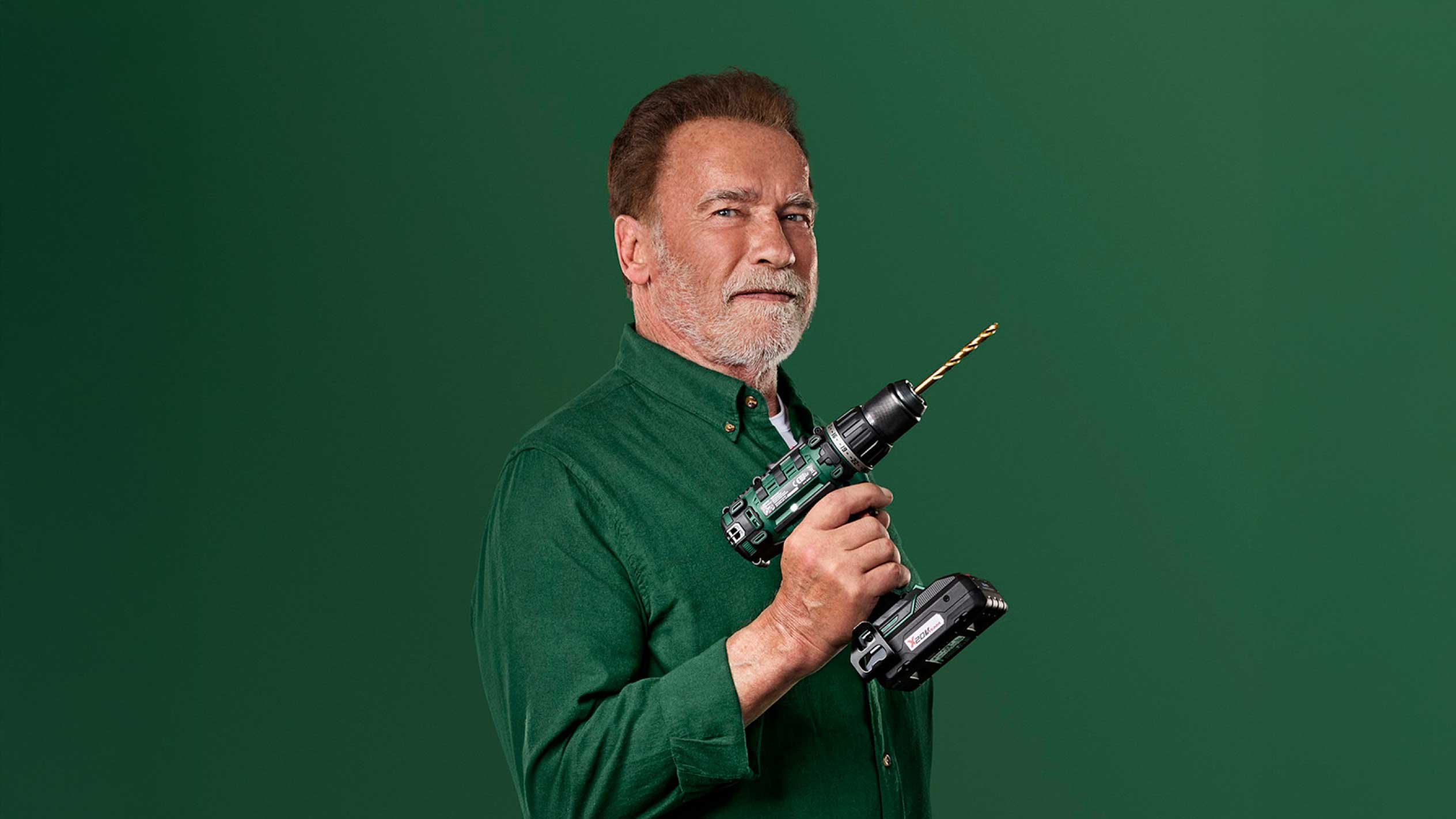 Arnold Schwarzenegger holder en grøn ledningsfri boremaskine med et guldbor.