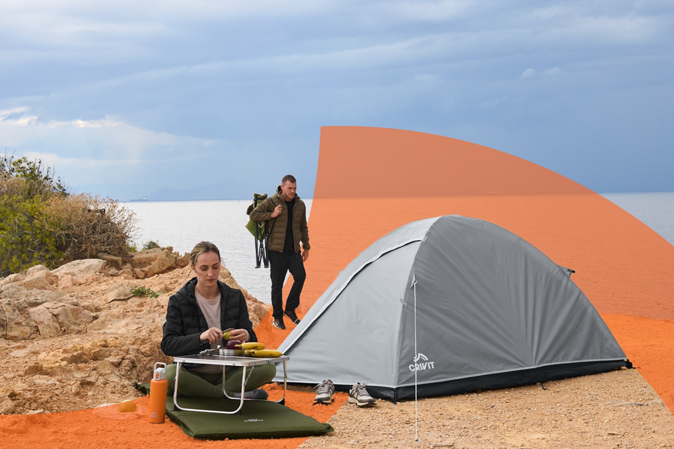 Et telt og en kvinde, der tilbereder mad ved et bord, mens en mand går i baggrunden.