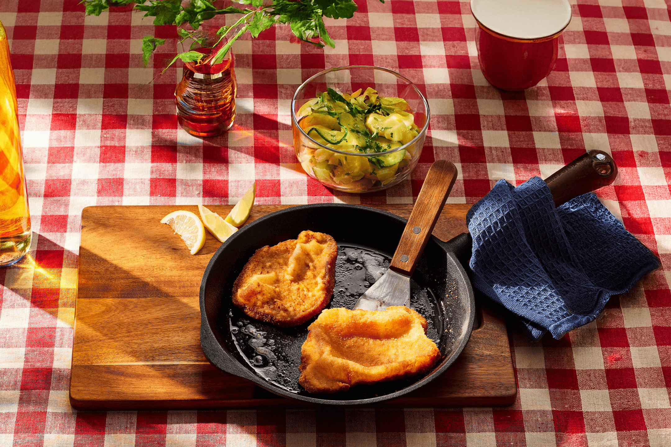 Stegt schnitzel i pande med agurkesalat, citron og en rødternet dug.