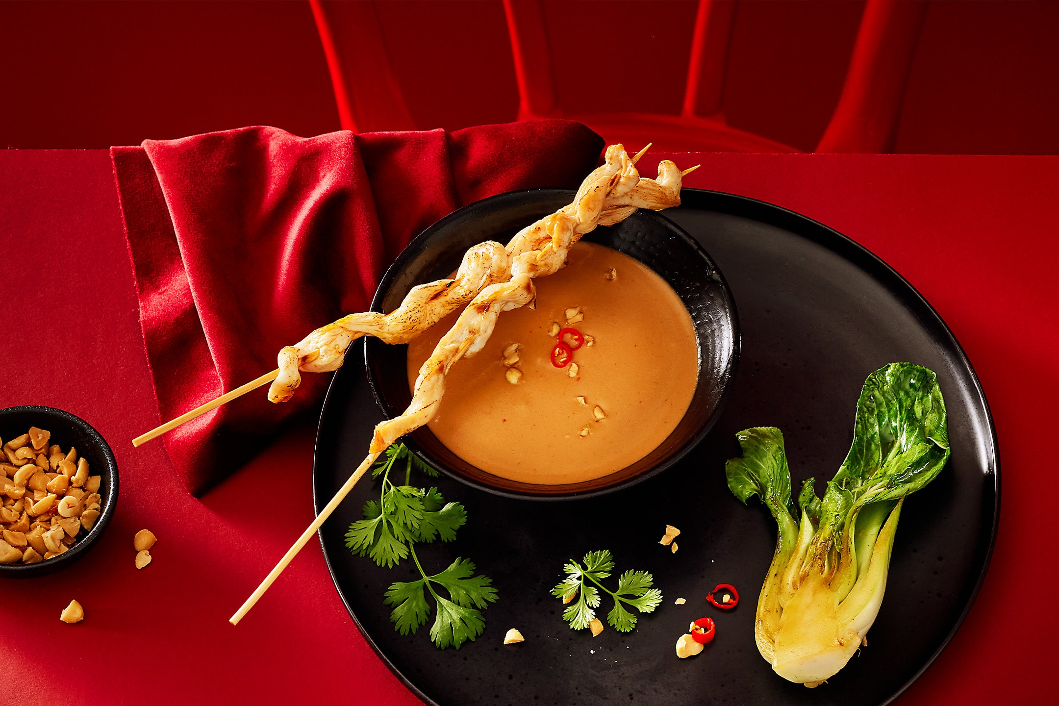 Kyllingespyd med jordnøddesauce, bok choy og koriander på en sort tallerken.