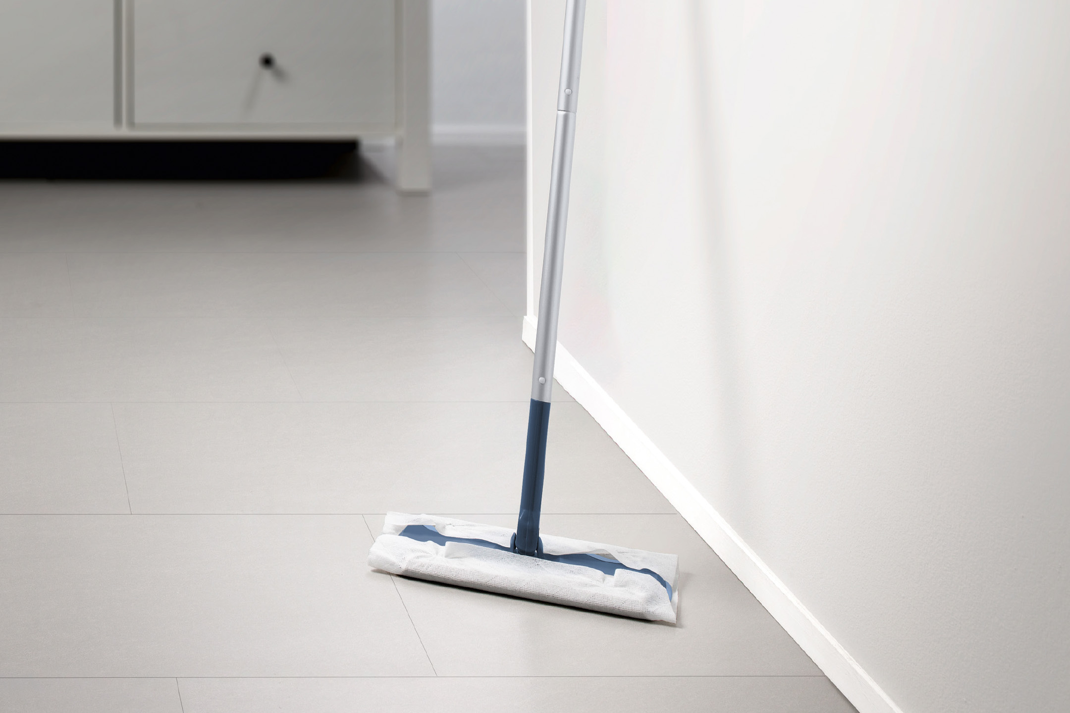 En gulvmoppe med engangsklud står op ad en hvid væg på et lyst gulv.