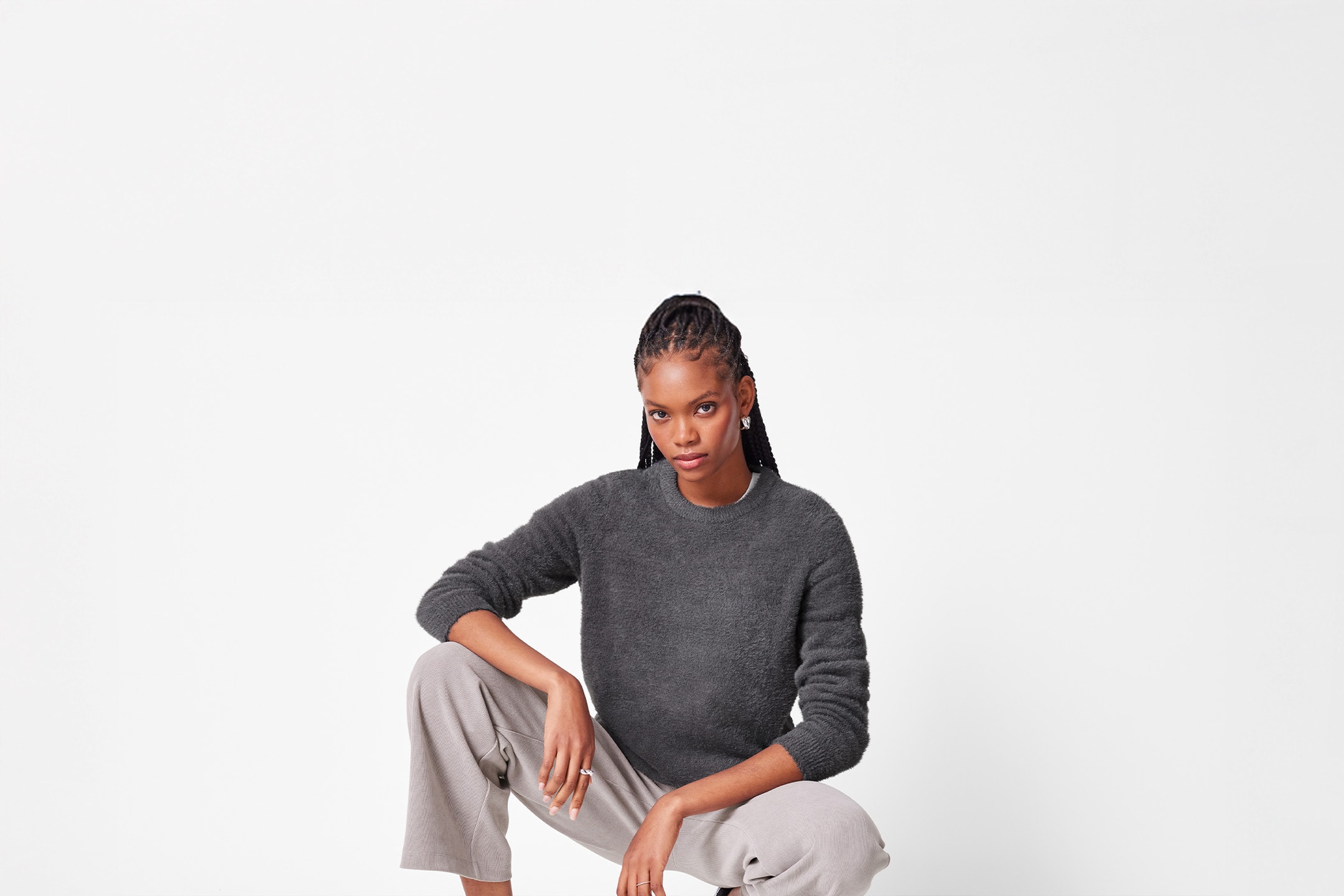 Kvinde i mørkegrå fluffy sweater og lysegrå bukser, der sidder på hug.