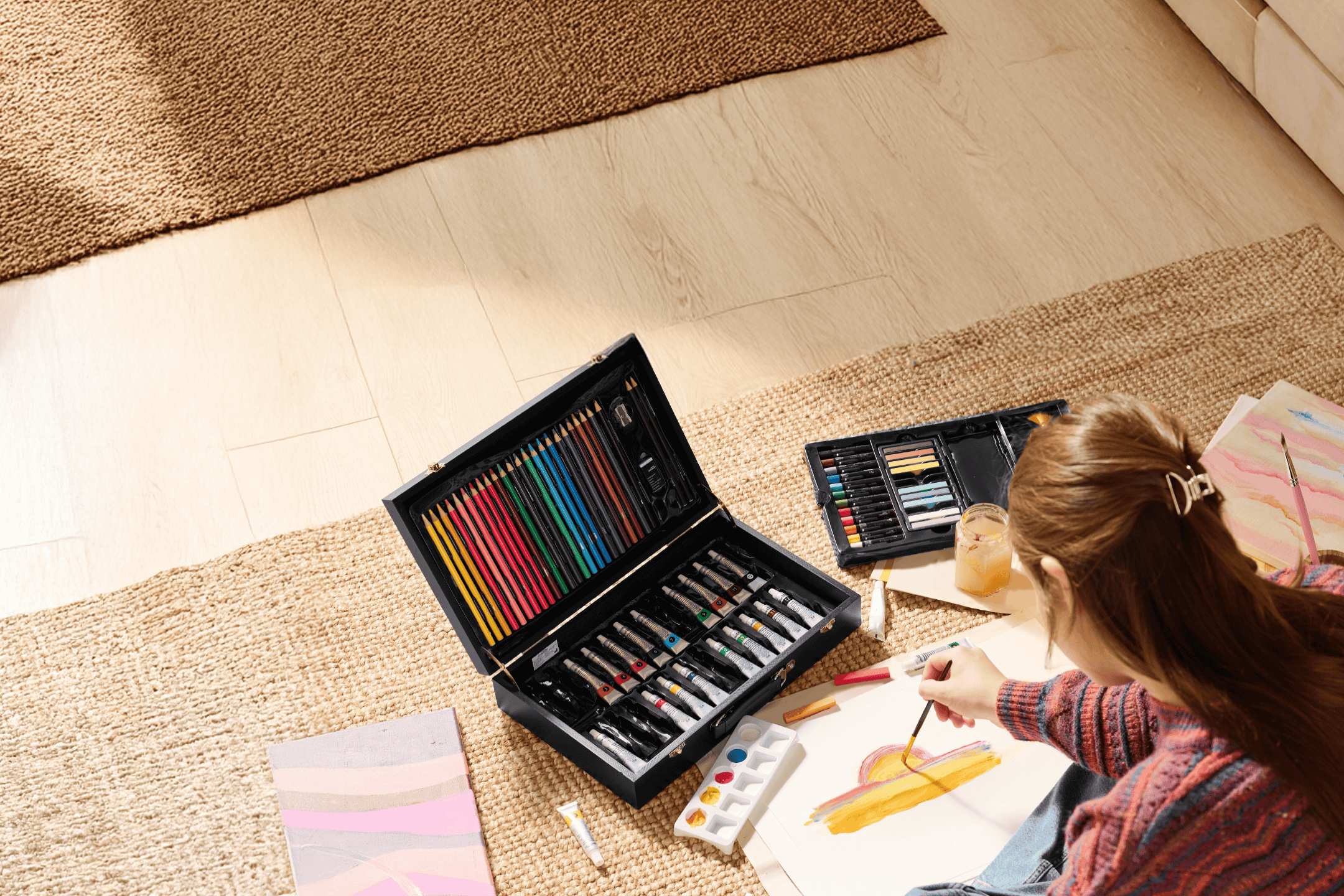 En person maler med et stort sæt kunstforsyninger, herunder farveblyanter og maling.