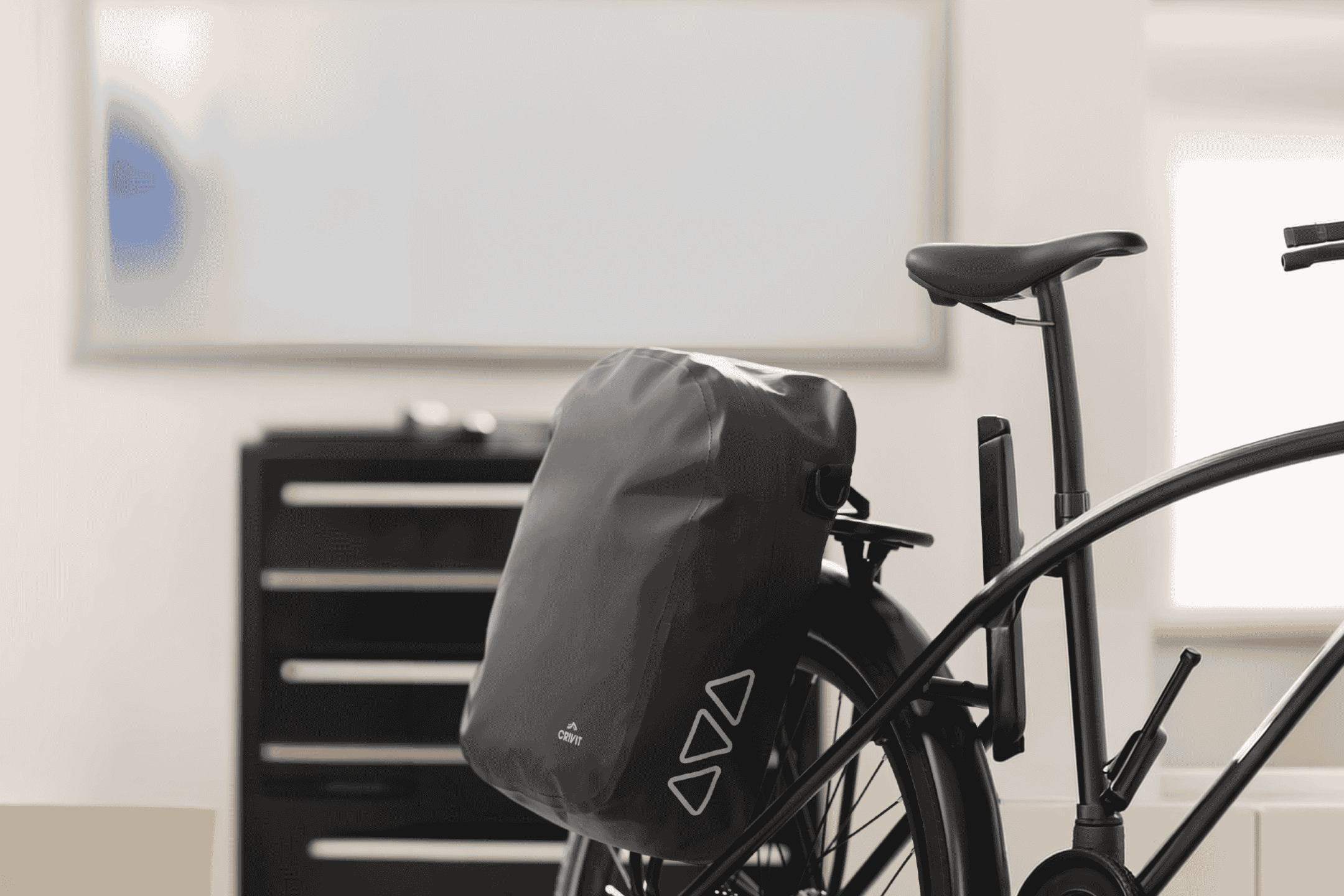 Sort cykeltaske på en cykel, med et hvidt whiteboard i baggrunden.