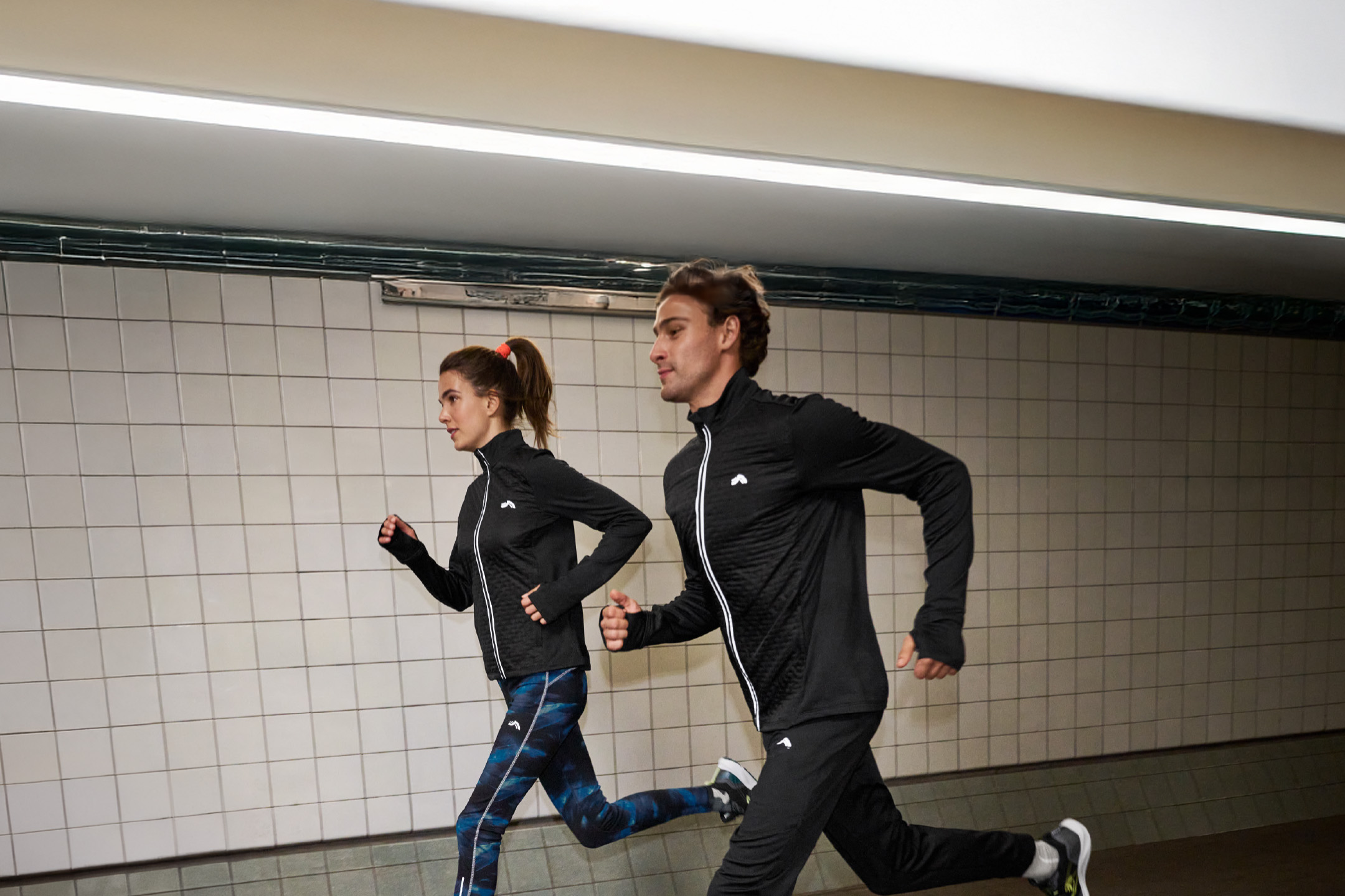 To personer i sort Crivit sportstøj løber i en underjordisk gang.