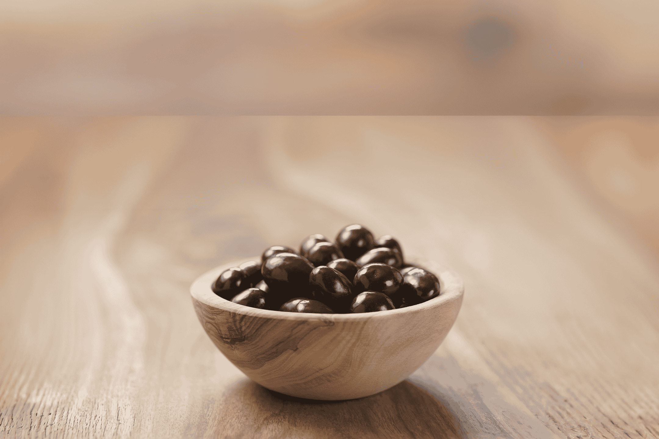 En træskål fyldt med mørke chokoladeovertrukne nødder på et træbord.