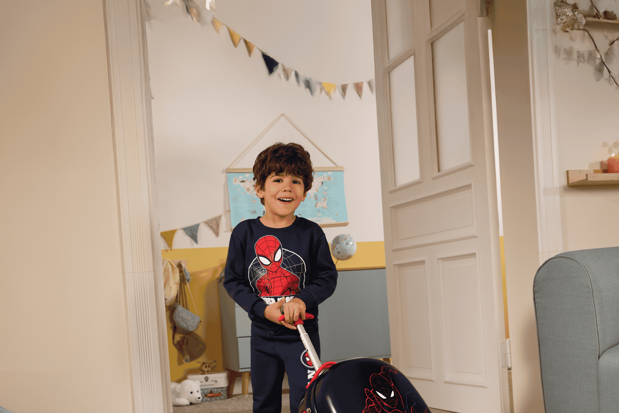 Glad dreng i pyjamas med Spiderman-motiv trækker en kuffert med Spiderman-motiv.