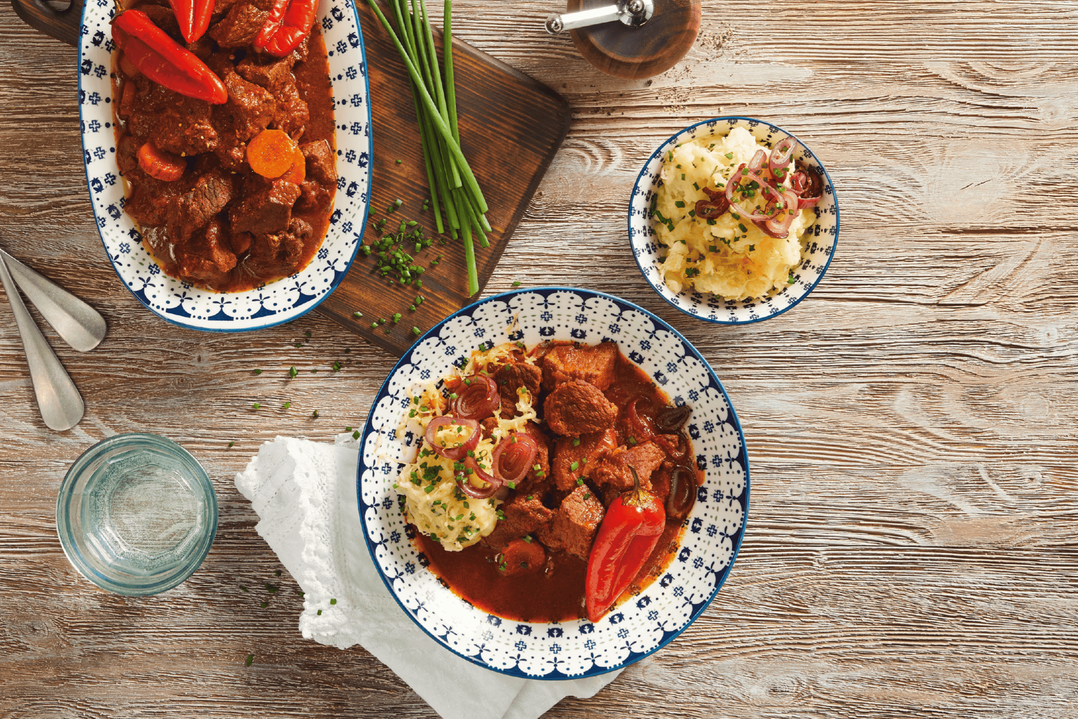 Gryderet med oksekød og peberfrugt serveret med kartoffelmos og rødløg på et træbord.
