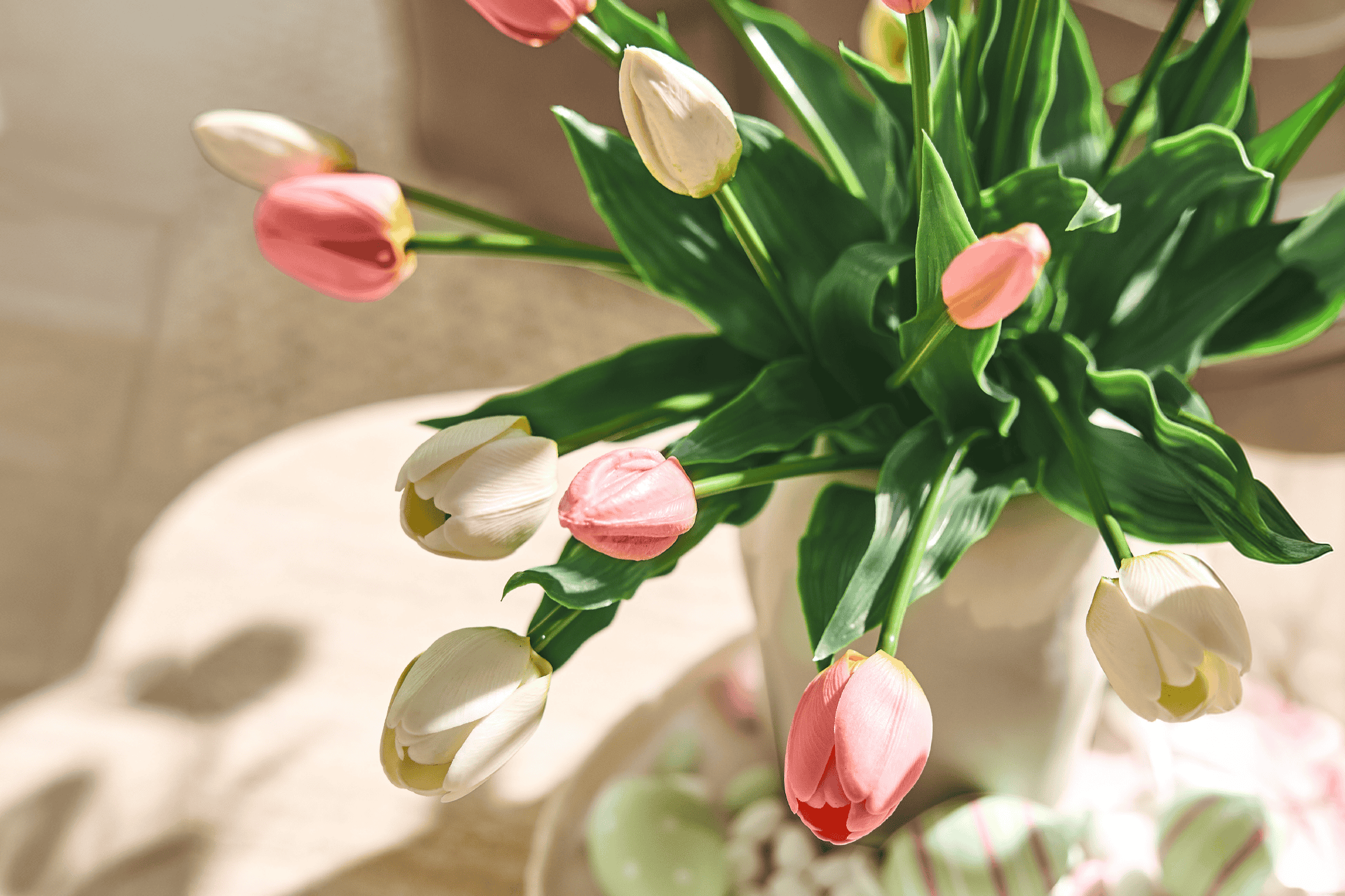 En buket lyserøde og hvide tulipaner i en vase, med påskeæg i baggrunden.