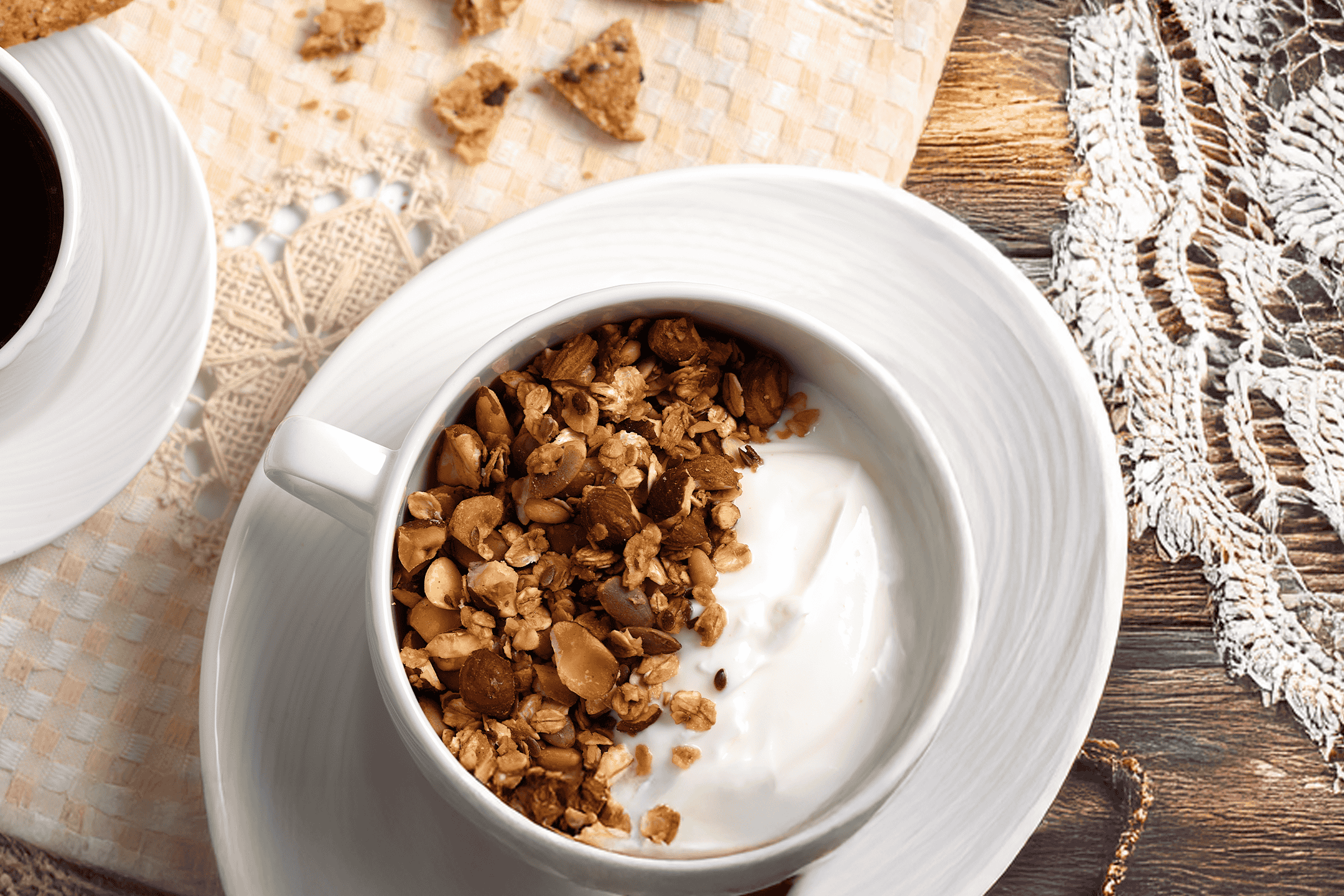 En skål med yoghurt og granola, en kop kaffe og småkager på et bord.