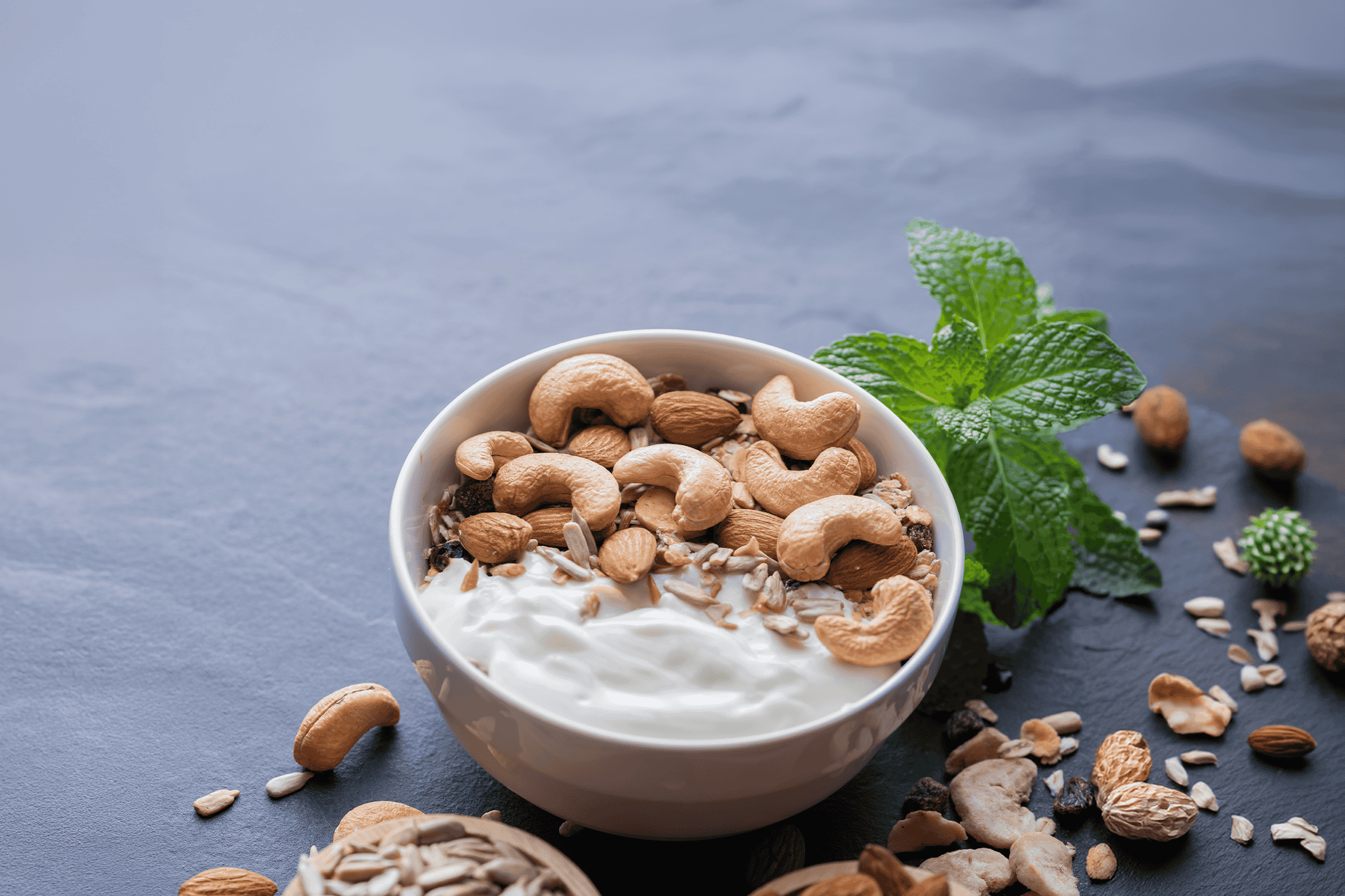 Skål med yoghurt, cashewnødder, mandler og granola på en mørk baggrund.