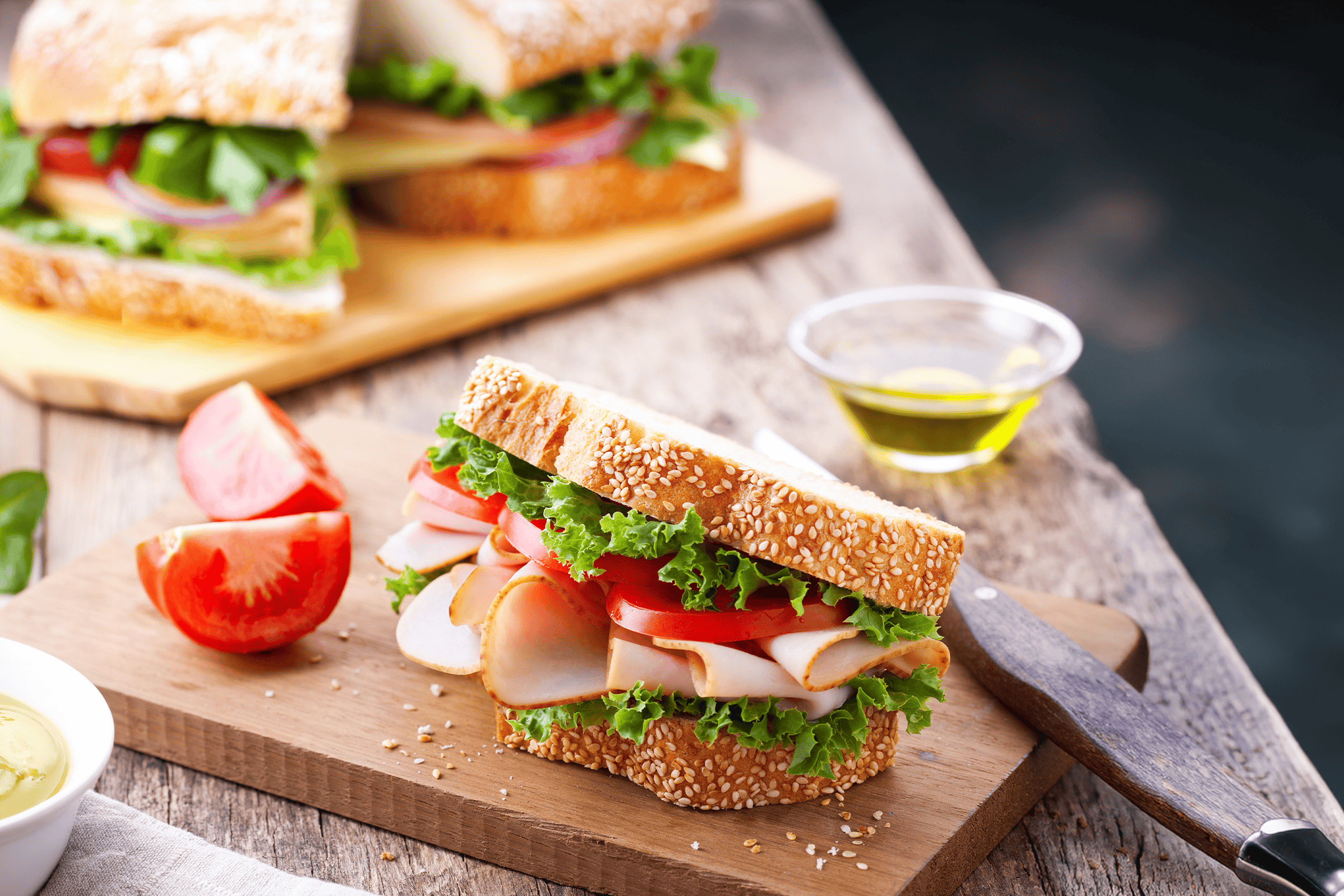 To kalkunsandwicher med salat og tomat på et træskærebræt.