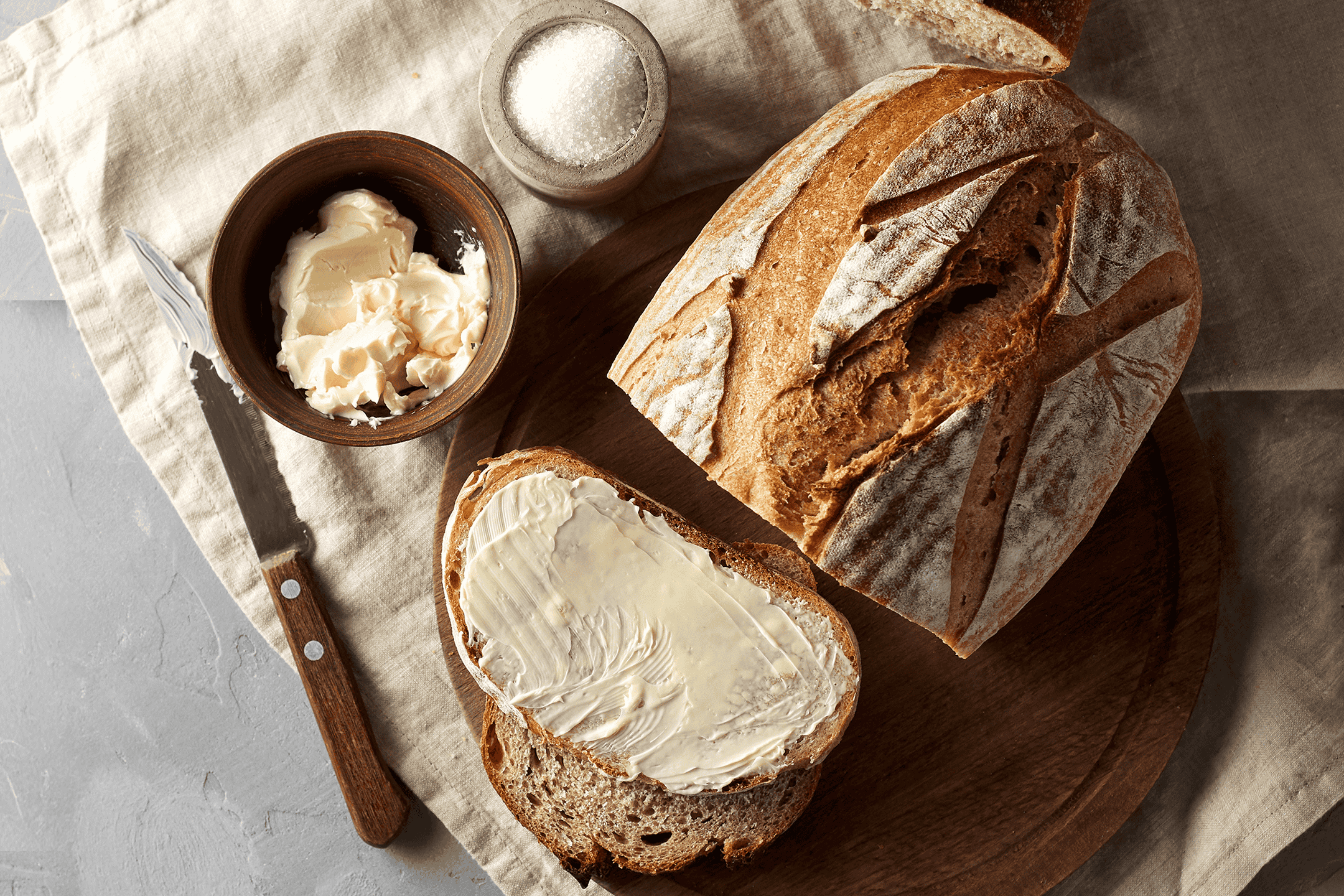 Friskbagt brød med smør og salt på et træskærebræt.
