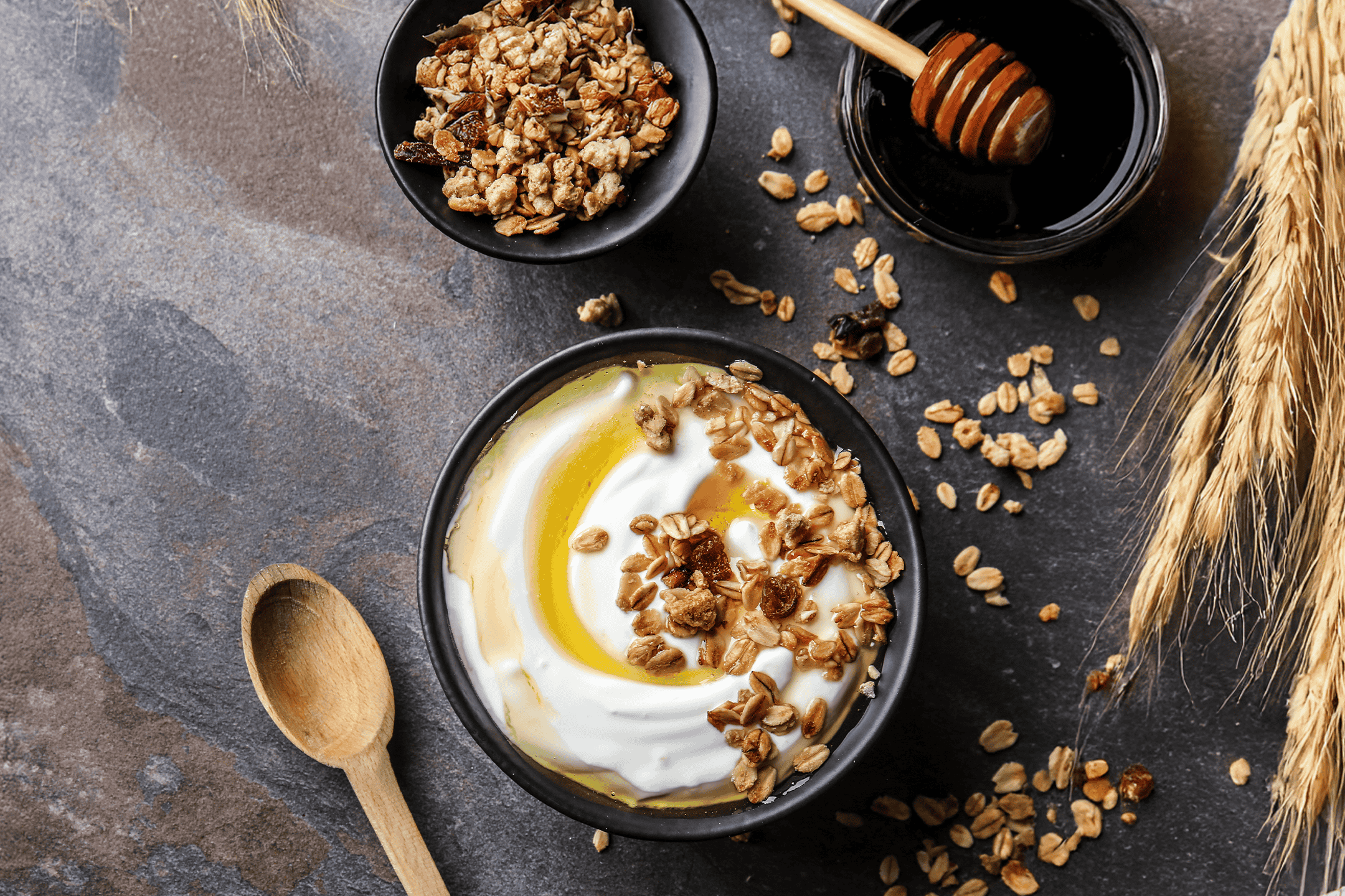 Græsk yoghurt med honning og granola i en sort skål, med en skål granola og honning ved siden af.