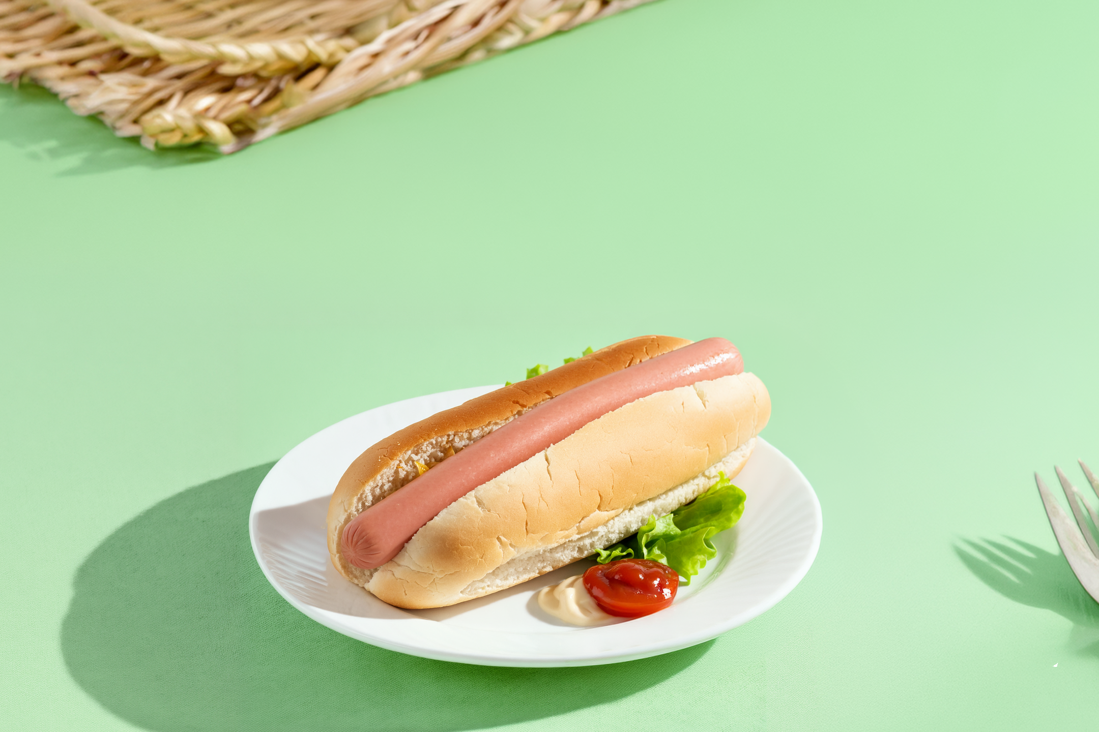 Hotdog med salat, ketchup og mayonnaise på en hvid tallerken på lysegrøn baggrund.