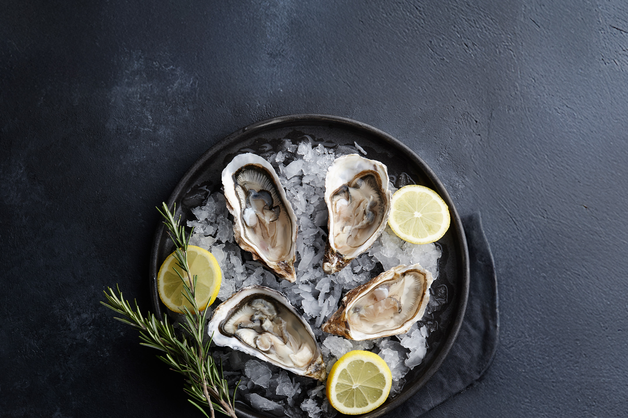 Friske østers på is med citron og rosmarin på en mørk baggrund.