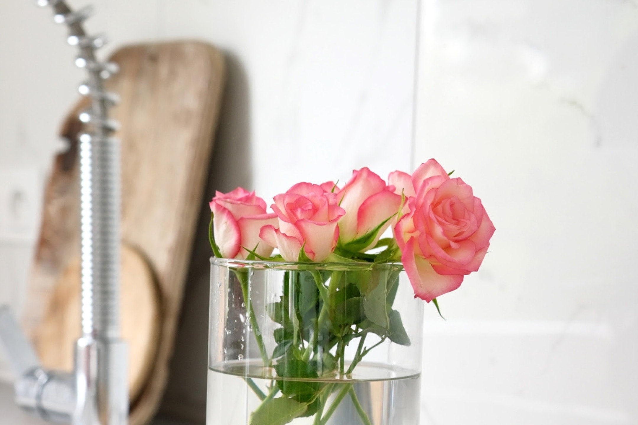 Pink roser i en vase på et køkkenbord med en vandhane i baggrunden.