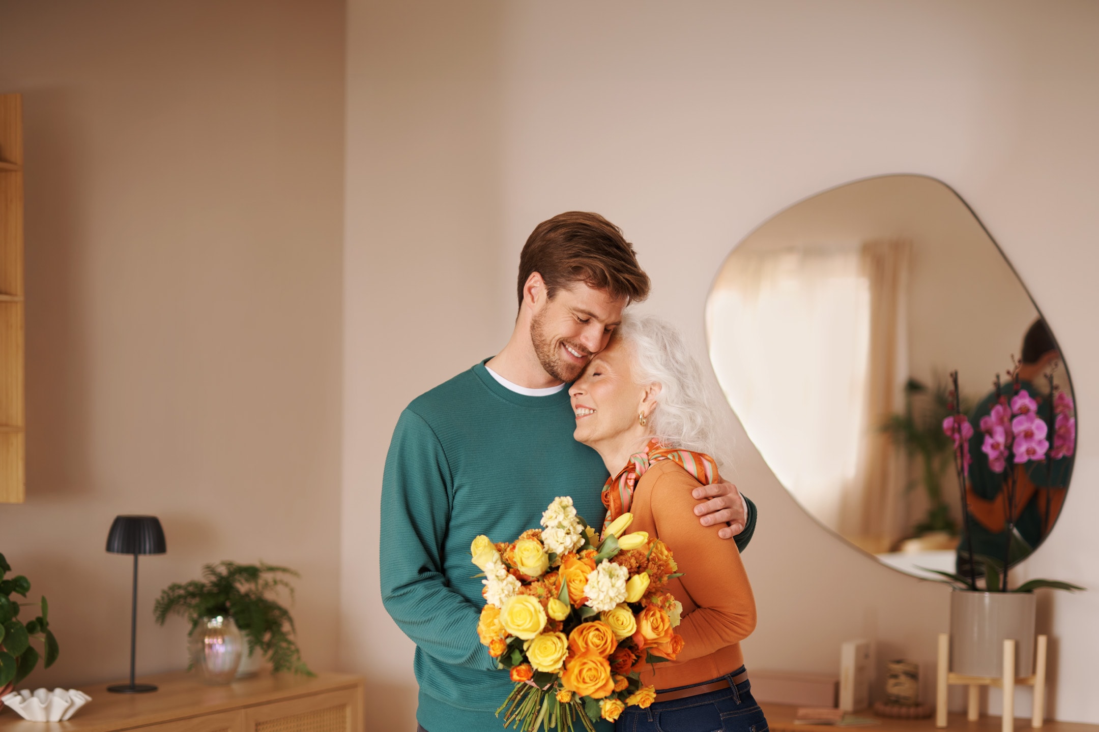 Mand og kvinde krammer med en buket gule og orange blomster.