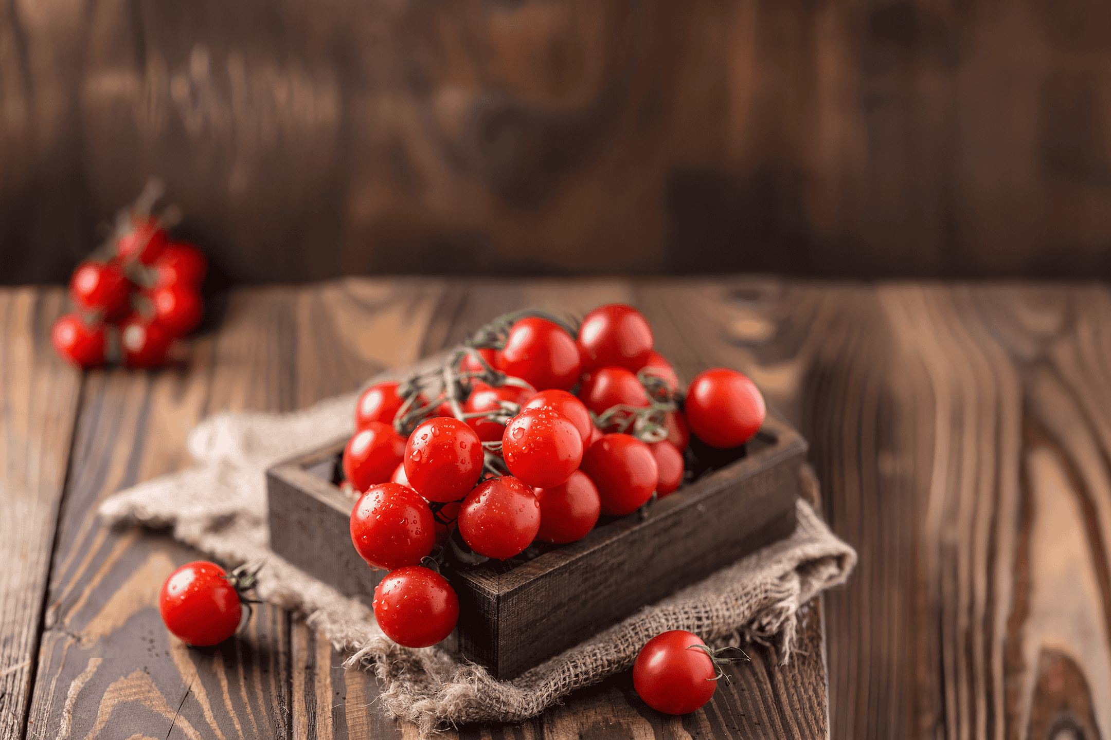 Friske cherrytomater med vanddråber i en trækasse på et træbord.