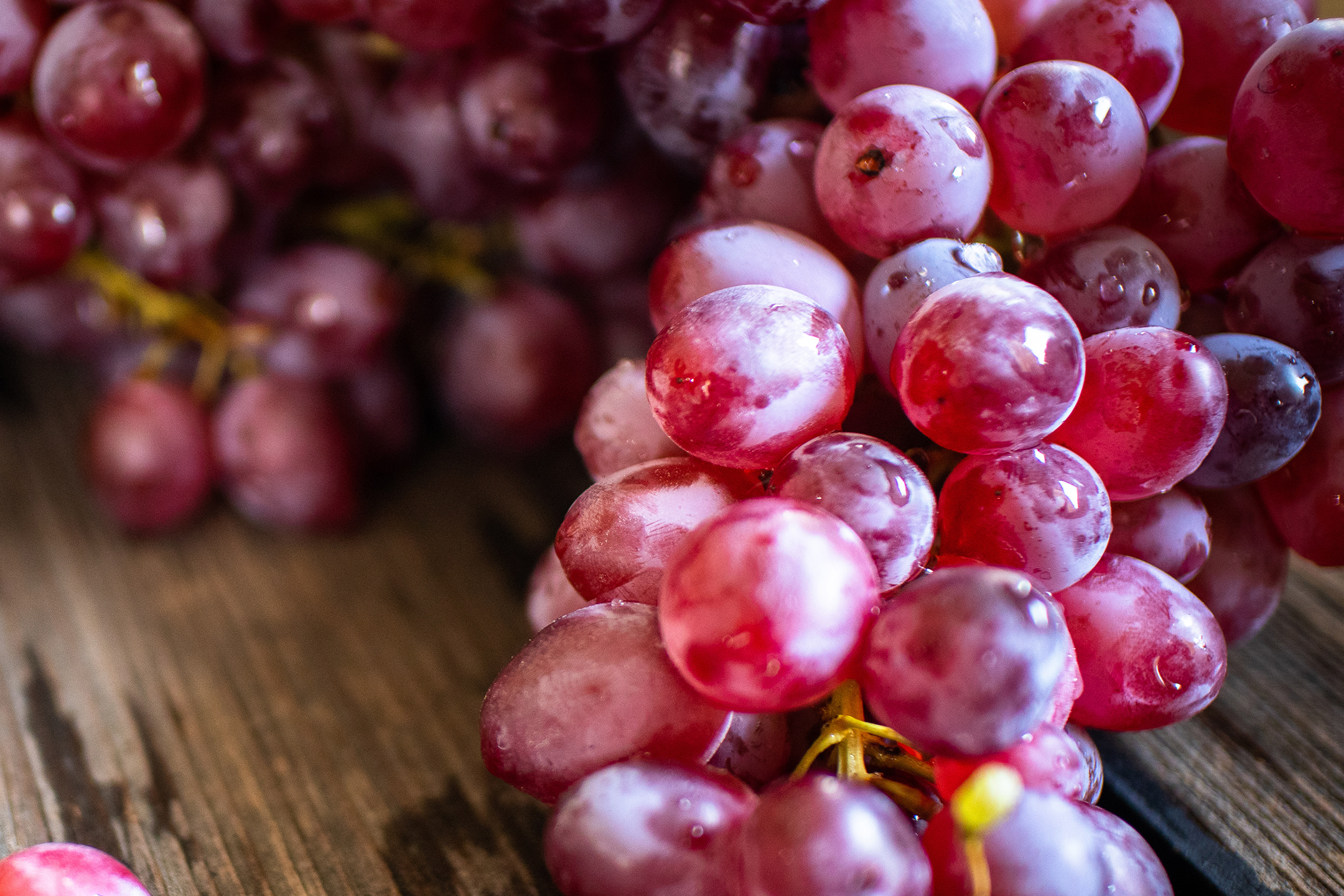 Nærbillede af friske røde druer med vanddråber på en træoverflade.
