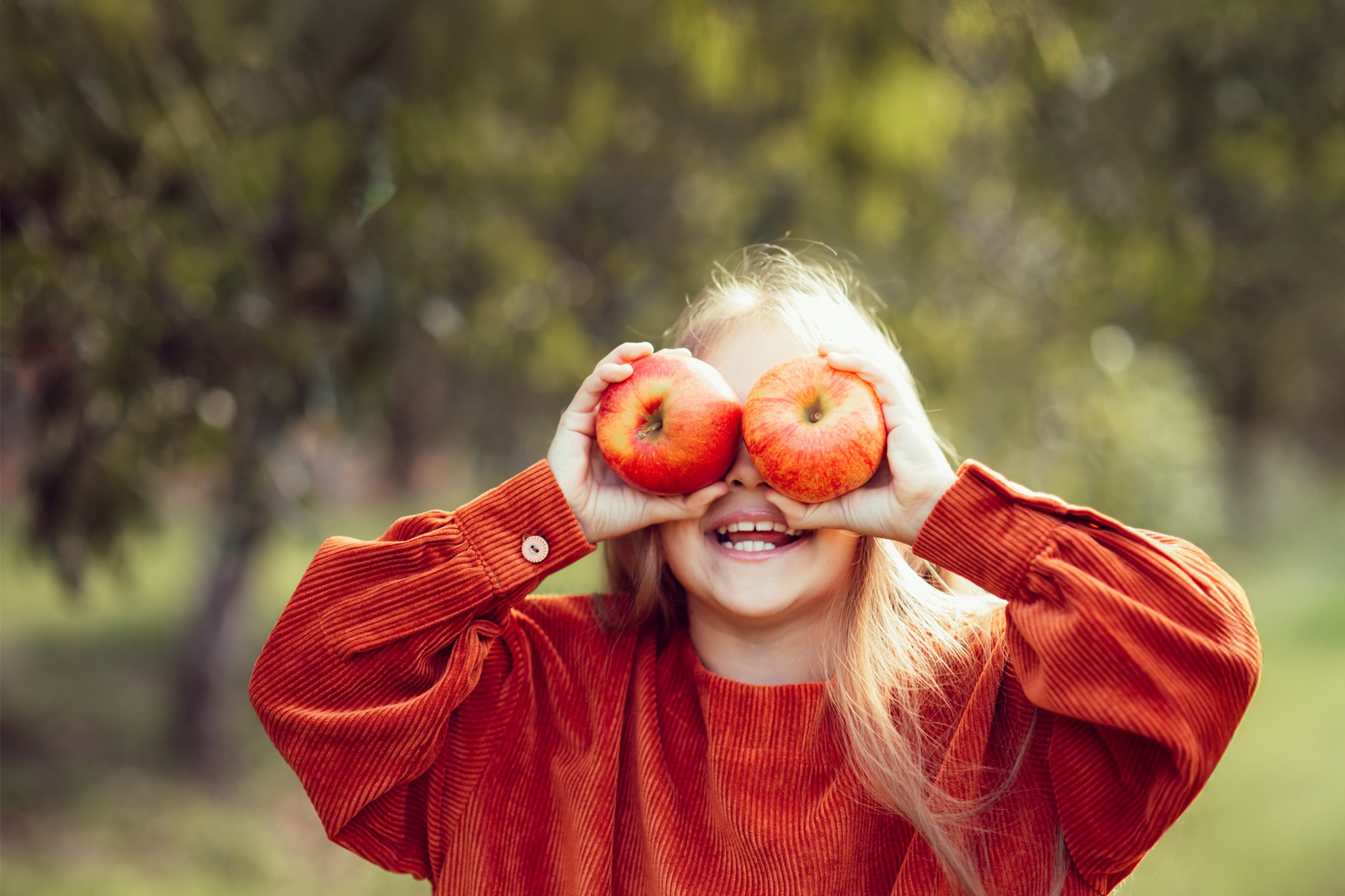 Glad pige i orange trøje holder to æbler foran øjnene.