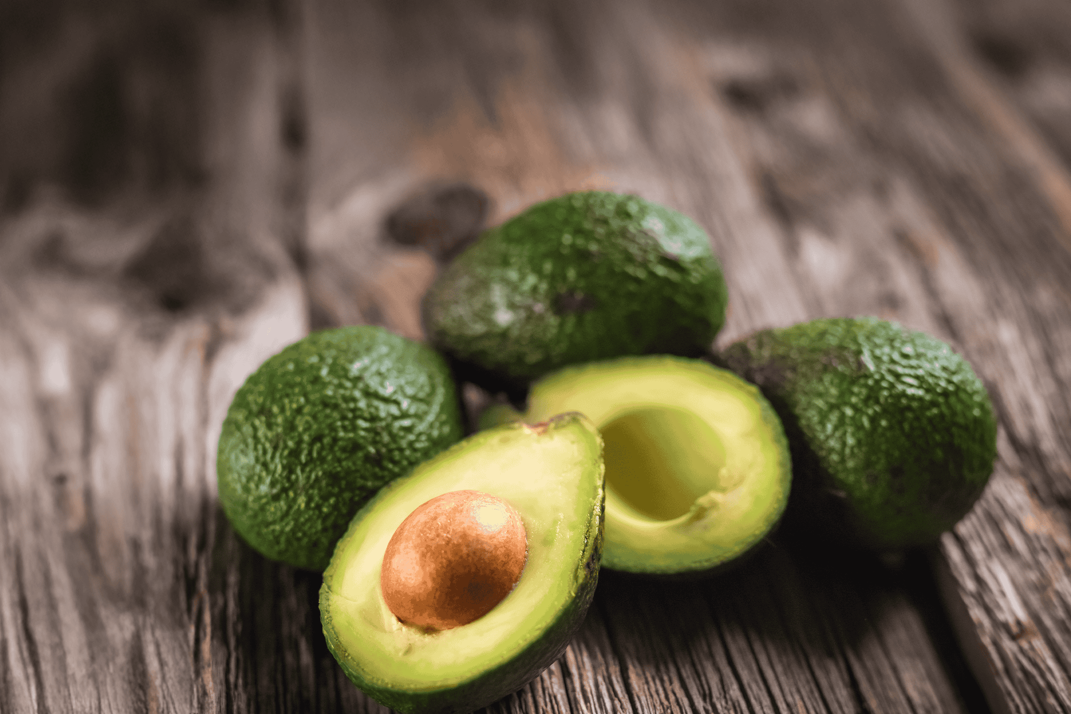 Friske, grønne avocadoer, hvoraf to er skåret over og viser den lysegrønne frugt og kerne.