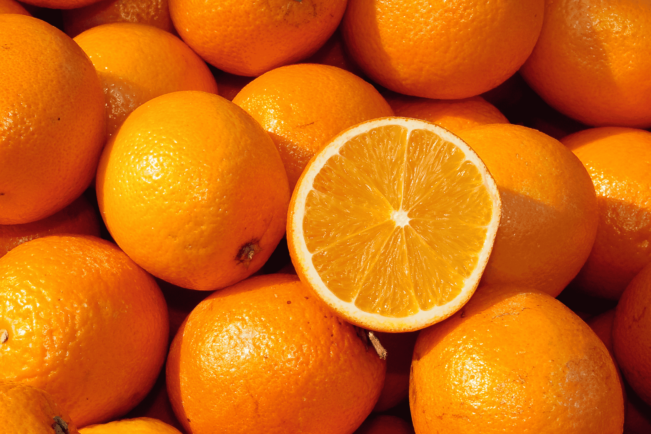 En bunke friske appelsiner, hvoraf én er skåret over og viser frugtkødet.