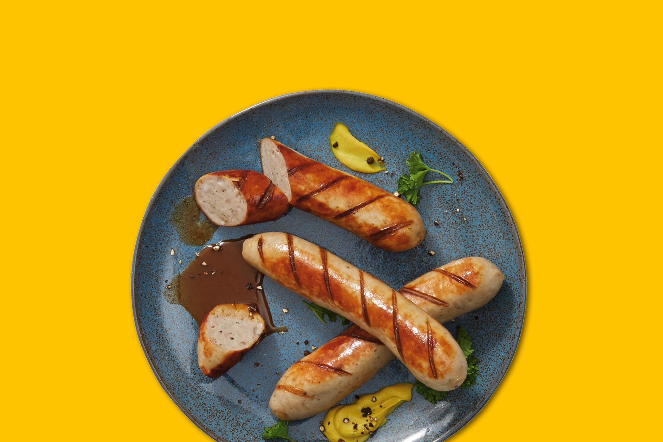 Grillede pølser med sennep og sovs på en blå tallerken.