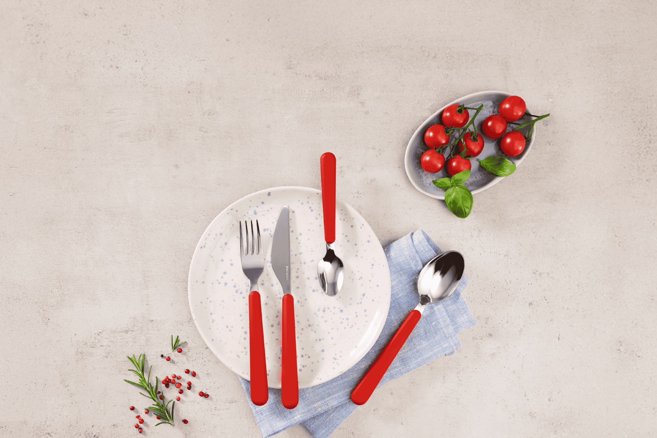 Bestiksæt med røde håndtag på en tallerken med tomater, basilikum og rosmarin.